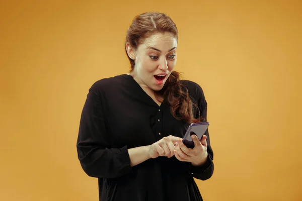 Mladá krásná žena pomocí mobilních telefonů studio na zlaté barvy pozadí — Stock fotografie