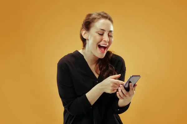 Mujer hermosa joven usando estudio de teléfono móvil sobre fondo de color oro — Foto de Stock