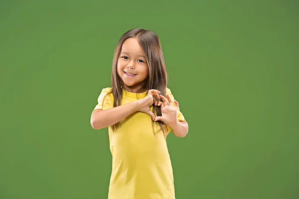 Linda menina adolescente sorridente faz a forma de um coração com as mãos no fundo verde . — Fotografia de Stock