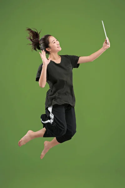 Зображення молодої жінки на зеленому тлі за допомогою ноутбука або планшетного пристрою під час стрибків . — стокове фото