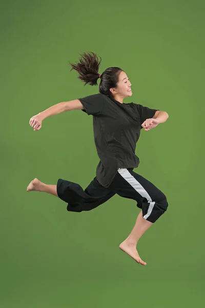 Vrijheid in beweging. Mooie jonge vrouw springen tegen groene achtergrond — Stockfoto