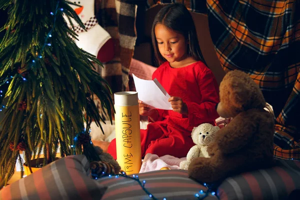 Καλά Χριστούγεννα και καλές γιορτές. Χαριτωμένο κορίτσι μικρό παιδί γράφει το γράμμα στον Άγιο Βασίλη κοντά στο χριστουγεννιάτικο δέντρο — Φωτογραφία Αρχείου