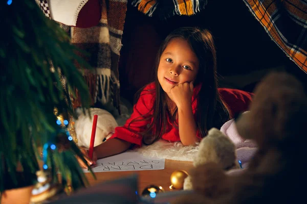 Feliz Navidad y Felices Fiestas. Linda niña escribe la carta a Santa Claus cerca del árbol de Navidad —  Fotos de Stock