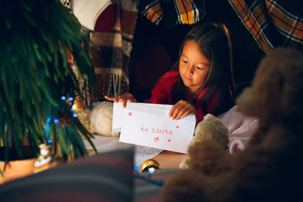 Καλά Χριστούγεννα και καλές γιορτές. Χαριτωμένο κορίτσι μικρό παιδί γράφει το γράμμα στον Άγιο Βασίλη κοντά στο χριστουγεννιάτικο δέντρο — Φωτογραφία Αρχείου