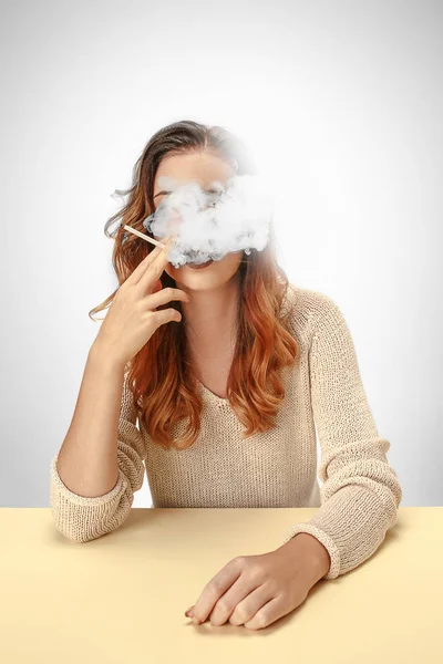 Mujer tranquila sentada y fumando descansando en la mesa. Nube de humo cubriendo su cara. Copiar espacio —  Fotos de Stock