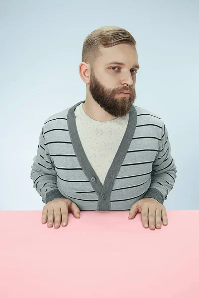 Serious business man sitting at a table on a blue background — Stock Photo, Image