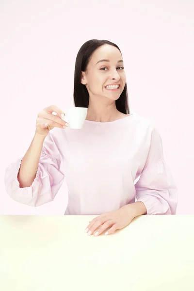 Hermosa mujer solitaria sentada en el estudio y mirando feliz sosteniendo la taza de café en la mano. Retrato de primer plano tonificado — Foto de Stock