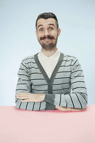 The happy smiling businessman sitting at a table on a blue background — Stock Photo, Image
