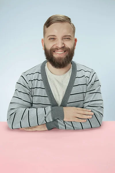Mavi bir arka plan üzerinde bir masada oturan mutlu gülümseyen iş adamı — Stok fotoğraf