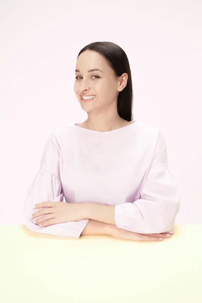 Die fröhliche und lächelnde Geschäftsfrau, die an einem Tisch auf rosa Hintergrund sitzt — Stockfoto