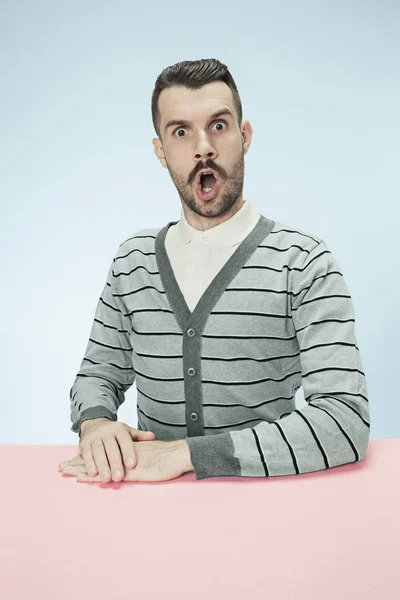 Hombre de negocios sorprendido sentado en una mesa sobre un fondo azul — Foto de Stock