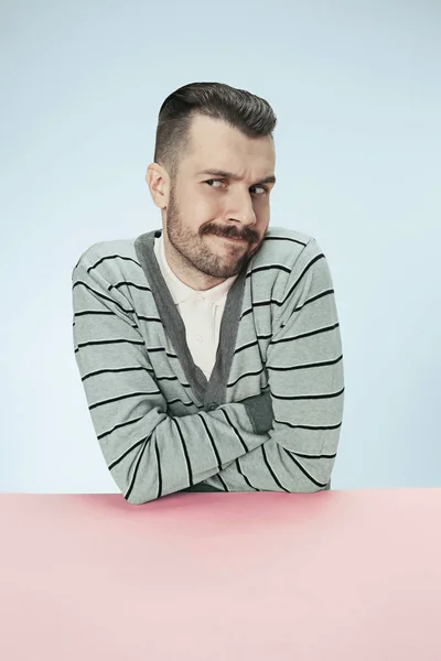 Serious suspicious business man sitting at a table on a blue background — Stock Photo, Image