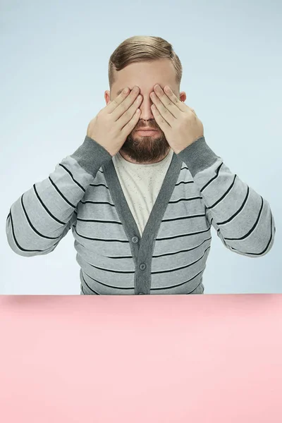 Joven sentado en la mesa en el estudio con los ojos cerrados aislados en azul — Foto de Stock