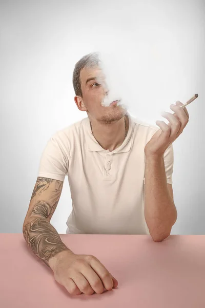 Hombre hipster guapo fumando cigarrillo en casa. Hombre mirando hacia arriba y disfrutando de pasar tiempo libre . — Foto de Stock