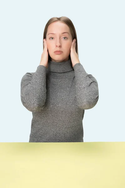 Porträt einer gestressten Frau, die mit geschlossenen Händen am Tisch sitzt und ihre Ohren mit Händen bedeckt. — Stockfoto