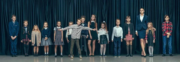 Bonito crianças elegantes no fundo do estúdio escuro. As meninas adolescentes bonitas e menino de pé juntos — Fotografia de Stock