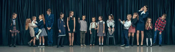 Bonito crianças elegantes no fundo do estúdio escuro. As meninas adolescentes bonitas e menino de pé juntos — Fotografia de Stock