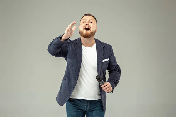 Young man with microphone on gray background, leading with microphone — Stock Photo, Image