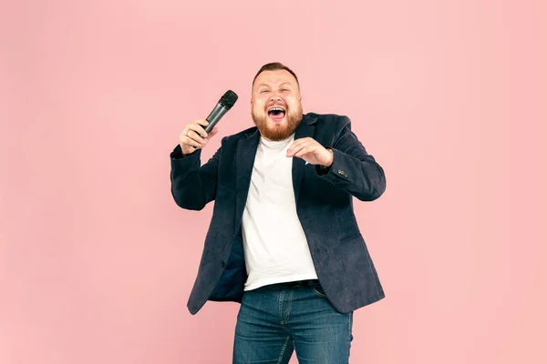 Junger Mann mit Mikrofon auf rosa Hintergrund, der mit Mikrofon führt — Stockfoto