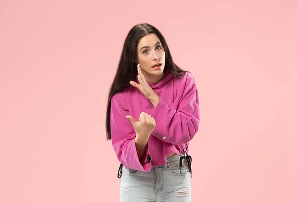Молодая женщина шепчет тайну за ее рукой на розовом фоне — стоковое фото