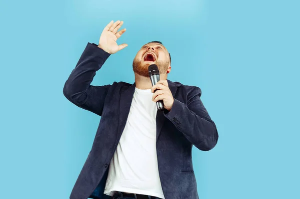 Hombre joven con micrófono sobre fondo azul, concepto principal — Foto de Stock