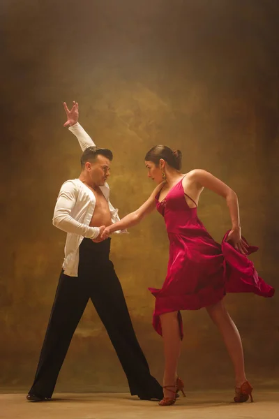 Tanzpaar in goldenem Kleid tanzt auf Studiohintergrund. — Stockfoto