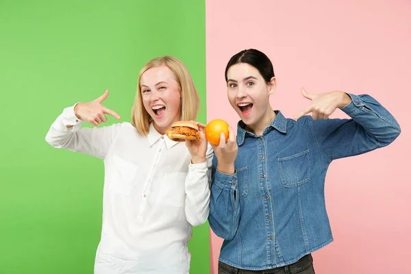 Dieta. Conceito de dieta. Comida saudável. Jovens mulheres bonitas escolhendo entre frutas e fast food desamparado — Fotografia de Stock