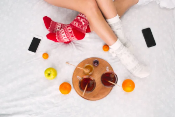 Mjuk bild av kvinna och man på sängen med telefon och frukter, högsta utsiktsplats. Kvinnliga och manliga ben i varma ull sockor — Stockfoto