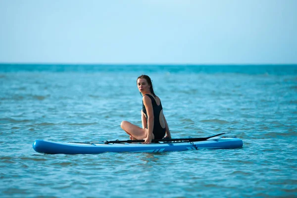 Joyeux jeune fille avec planche à pagaie sur la plage. Mer bleue en arrière-plan. Concept vacances d'été . — Photo