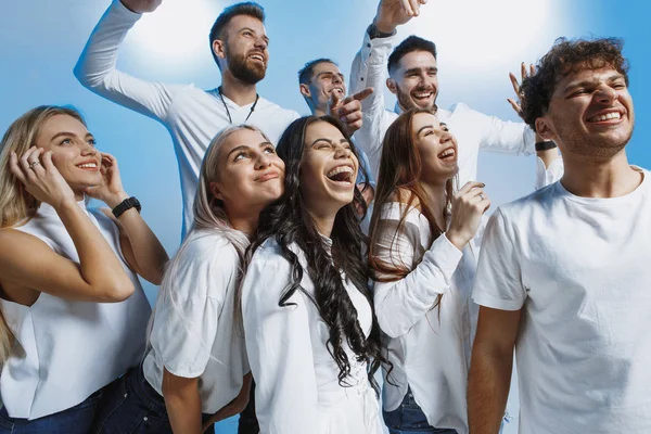 Gruppe fröhlich fröhlicher junger Leute steht und feiert gemeinsam vor blauem Hintergrund — Stockfoto