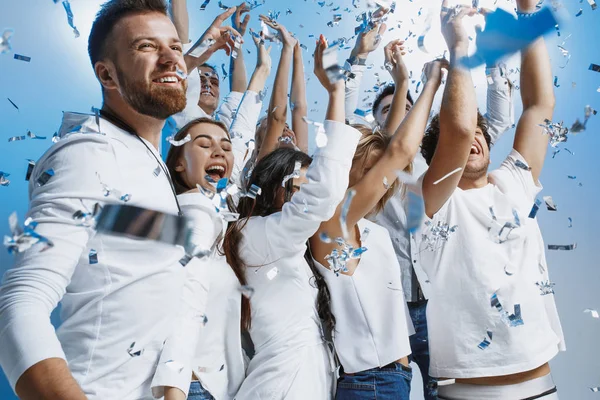 Grupo de jovens alegres alegres de pé e comemorando juntos sobre fundo azul — Fotografia de Stock