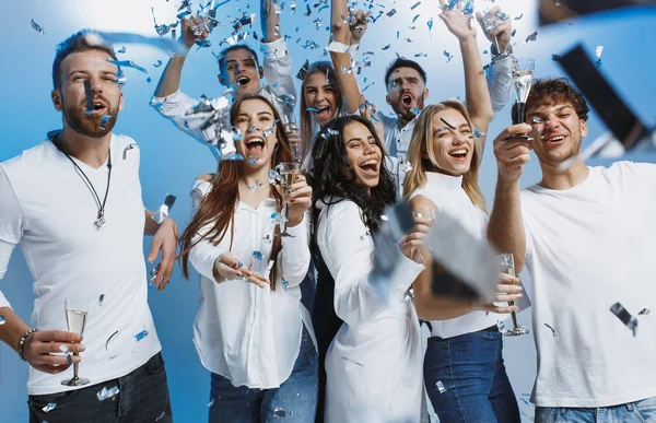 Grupo de jovens alegres alegres de pé e comemorando juntos sobre fundo azul — Fotografia de Stock