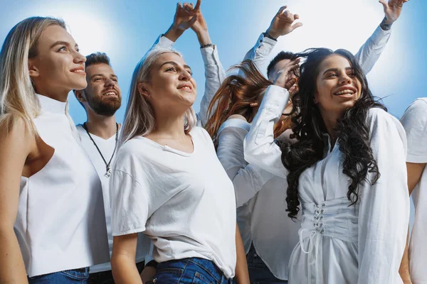 Grupo de jóvenes alegres y alegres de pie y celebrando juntos sobre fondo azul — Foto de Stock