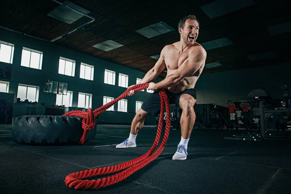 Uomo senza maglietta capovolgendo pneumatico pesante in palestra — Foto Stock