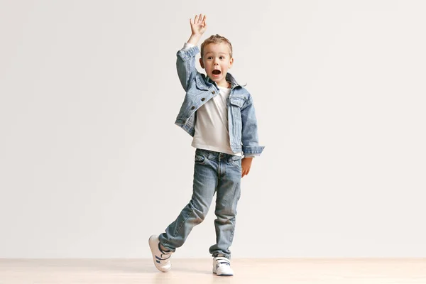 Портрет милого мальчика в стильной джинсовой одежде, смотрящего в камеру в студии — стоковое фото