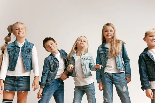 O retrato de menino e meninas bonitos em roupas de jeans elegantes olhando para a câmera no estúdio — Fotografia de Stock