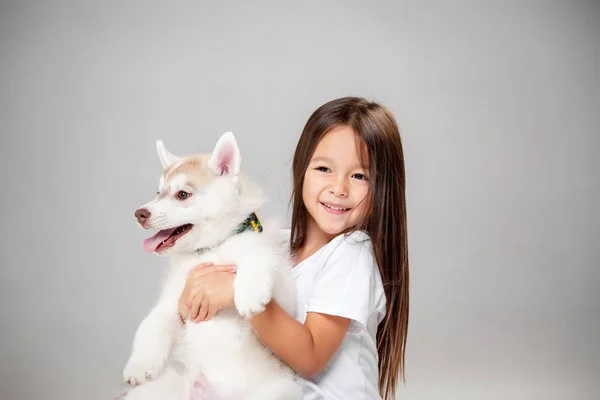 Retrato de uma menina alegre se divertindo com filhote de cachorro husky siberiano no chão no estúdio — Fotografia de Stock