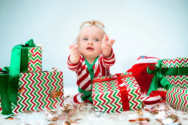 Χαριτωμένο μωρό κορίτσι 1 χρονών κοντά σε santa καπέλο ποζάρει πάνω από Χριστούγεννα φόντο. Κάθεται στο πάτωμα με Χριστουγεννιάτικη μπάλα. Περίοδος διακοπών. — Φωτογραφία Αρχείου