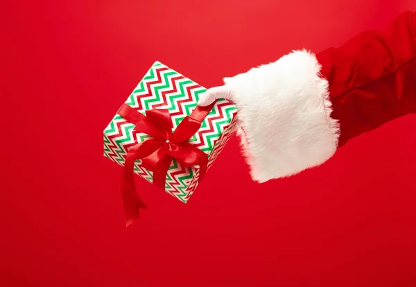 Mão de Papai Noel segurando um presente no fundo vermelho — Fotografia de Stock