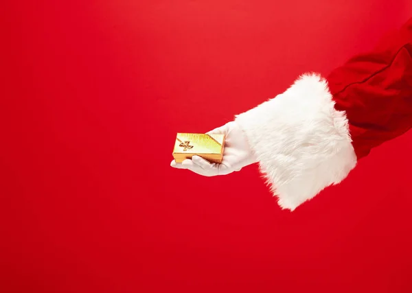 Hand av Santa Claus håller en gåva på röd bakgrund — Stockfoto
