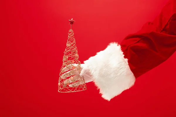 Mão de Papai Noel segurando uma árvore de Natal de brinquedo no fundo vermelho — Fotografia de Stock