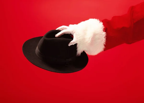 Mano de Santa Claus sosteniendo un sombrero masculino sobre fondo rojo — Foto de Stock