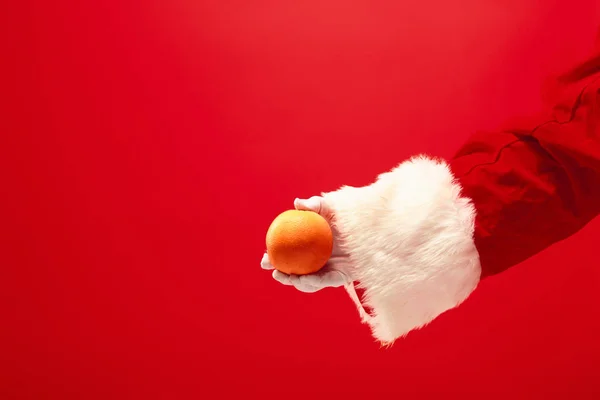 Hand des Weihnachtsmannes hält eine Orange auf rotem Hintergrund — Stockfoto