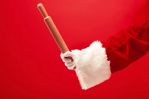 Ręka Świętego Mikołaja, trzymając kulinarne wałkiem na czerwonym tle — Zdjęcie stockowe