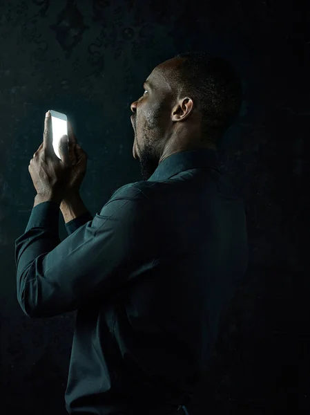 Студийный кадр молодого серьезного чернокожего африканца, думающего, разговаривая по мобильному телефону на черном фоне — стоковое фото
