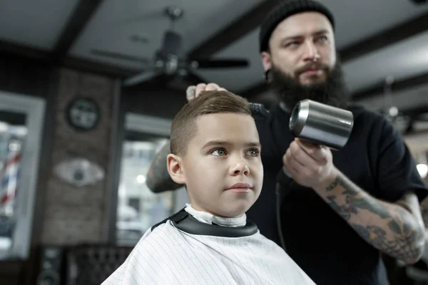 Kinder-Friseur schneidet kleinen Jungen vor dunklem Hintergrund. — Stockfoto
