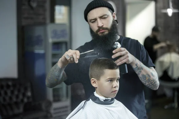 Children hairdresser cutting little boy against a dark background. — Stock Photo, Image