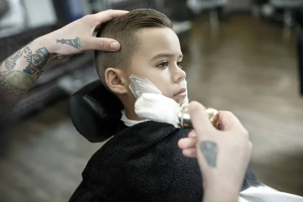 Children hairdresser cutting little boy against a dark background. — Stock Photo, Image