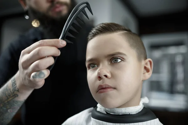 Coiffeur enfants coupant petit garçon sur un fond sombre . — Photo