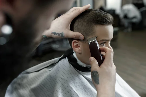 Coiffeur enfants coupant petit garçon sur un fond sombre . — Photo